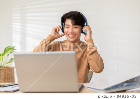 Entrepreneur handsome business asian man wear casual shirt and earphone listen having fun with music.Happy freelance wear wireless headphones dancing on desk at home during take a break 84936705