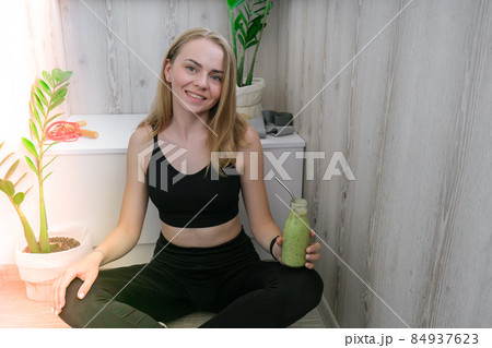Young millenial blond woman drinking vegan smoothie drink detox. Woman doing yoga exercises at home. Clean eating, weight loss, healthy dieting food concept. Stay healthy 84937623
