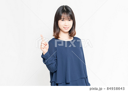 白い背景の前にたって、ポイントを示す若い女性 84938643