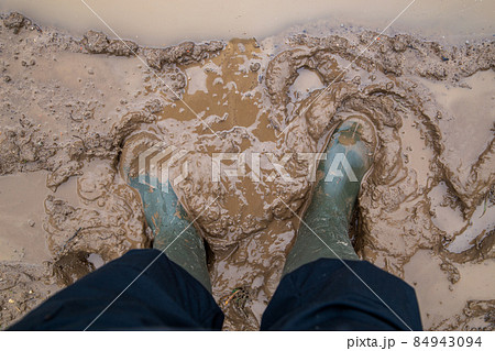 feet in green rubber boots stands in wet brown mud directly above view feet in green rubber boots stands in wet brown mud directly above view 84943094