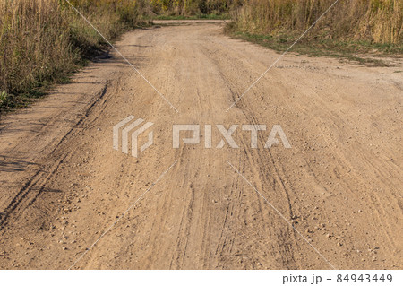 dusty dry dirt road with wild grass thickets on its sides 84943449