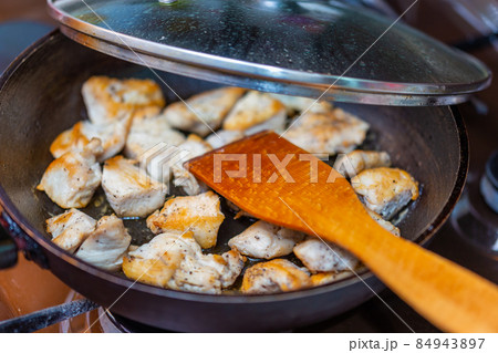 fried chicken in a open pan with ground black pepper and wooden kitchen spatula 84943897