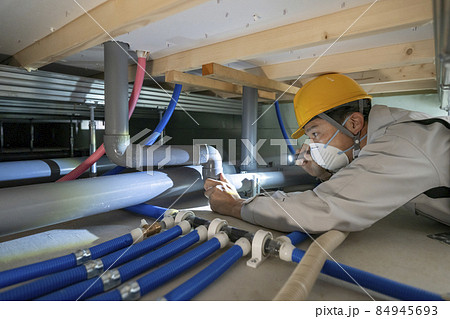 住宅の床下の排水管を点検する作業服の男性 84945693