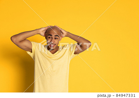 Emotional dark skinned man in t-shirt posing isolated on yellow color studio background. Concept of human emotions Emotional dark skinned man in t-shirt posing isolated on yellow color studio background. Concept of human emotions 84947331