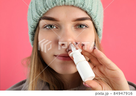 Young woman using nasal spray on pink background, runny nose concept 84947916