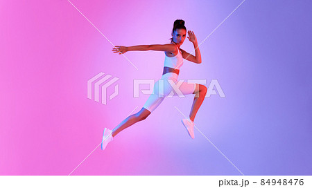 Athletic Female Jumping In Mid-Air Over Pink And Blue Background 84948476