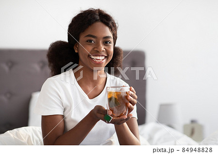 Happy african american lady drinking tea in bed Happy african american lady drinking tea in bed 84948828