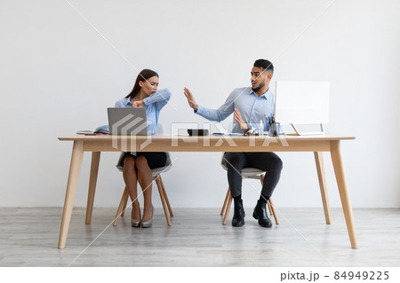 Female employee coughing in elbow near scared colleague Female employee coughing in elbow near scared colleague 84949225