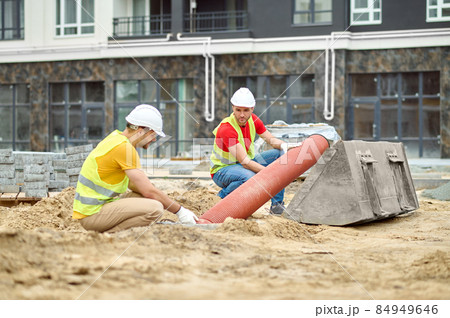 Two men crouched near pipe at construction site 84949646