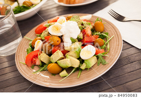fresh salad of arugula, avocado, cherry tomatoes with olives and quail eggs on brown plate fresh salad of arugula, avocado, cherry tomatoes with olives and quail eggs on brown plate 84950083