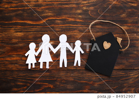 Happy paper cut family holding hands on wooden background near little toy house Happy paper cut family holding hands on wooden background near little toy house 84952907