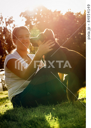 A happy teenage girl sits on a lawn and plays with a dog to hug him 84954149