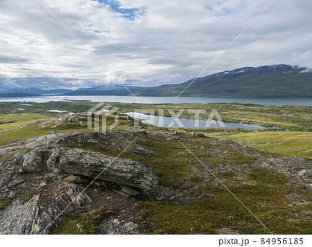 Lapland landscape at Virihaure lake with winding river, green mountains, birch trees and plain with big boulders. Sweden summer cloudy day, wild nature, Padjelantaleden hiking trail. 84956185