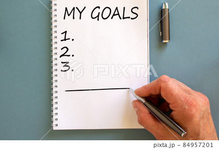Male hand writing 'my goals' on white note, isolated on blue background. 84957201