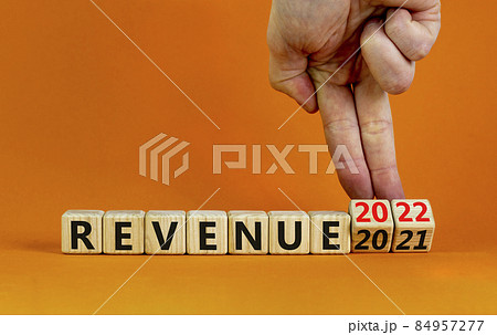 2022 revenue new year symbol. Businessman turns a wooden cube and changes words 'revenue 2021' to 'revenue 2022'. Beautiful orange background, copy space. Business, 2022 revenue new year concept. 84957277