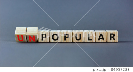 Popular or unpopular symbol. Turned wooden cubes and changed the word unpopular to popular. Beautiful grey table, grey background. Popular or unpopular and business concept. Copy space. 84957283