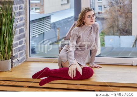 Myopia glasses on an 18 years old woman sitting on windowsill. Myopia glasses on an 18 years old woman sitting on windowsill. 84957610