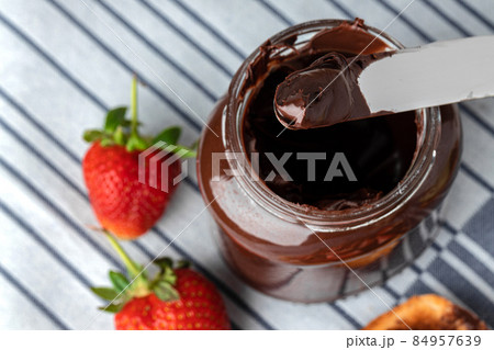 Top view of knife in chocolate paste with strawberries on white napkin 84957639