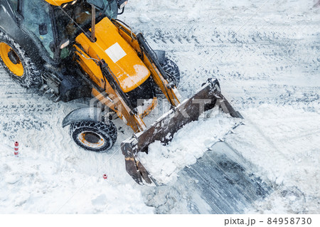 Tractor loader machine uploading dirty snow into dump truck. Cleaning city street, removing snow and ice after heavy snowfalls and blizzard. Snowplow outdoors clean pavement sidewalk road driveway Tractor loader machine uploading dirty snow into dump truck. Cleaning city street, removing snow and ice after heavy snowfalls and blizzard. Snowplow outdoors clean pavement sidewalk road driveway 84958730