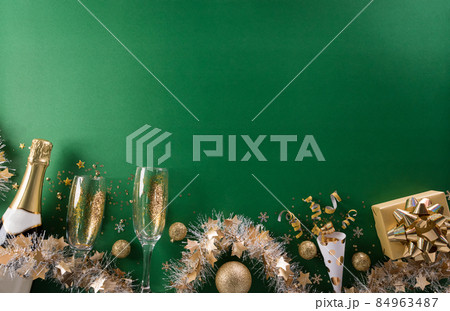 Happy New year celebration background concept. Champagne with glass, golden ribbon, stars and christmas ball on green background. Happy New year celebration background concept. Champagne with glass, golden ribbon, stars and christmas ball on green background. 84963487