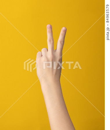 Woman hand shows two finger on yellow background Woman hand shows two finger on yellow background 84963579