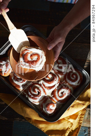 A man lays out homemade cinnabons buns on a plate of baking dish. Top view. A man lays out homemade cinnabons buns on a plate of baking dish. Top view. 84967294