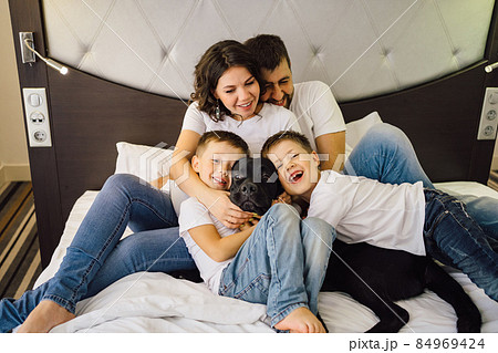 pregnant mother, father and two sons in jeans and white t-shirts on bed. pregnant mother, father and two sons in jeans and white t-shirts on bed. 84969424