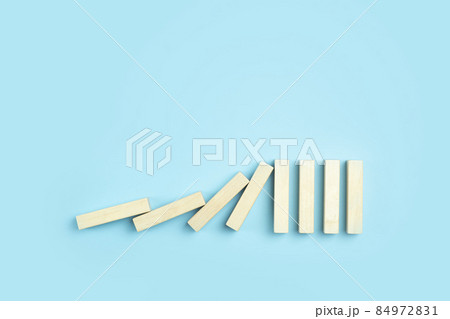 Falling pieces of dominoes on a clean blue minimal background. Business, risk, management and finance concept. Falling pieces of dominoes on a clean blue minimal background. Business, risk, management and finance concept. 84972831