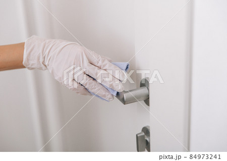 Cleaning door handle with blue wipe in white gloves. Woman hand using towel for cleaning home room door link. Sanitize surfaces prevention in hospital and public spaces against corona virus. Cleaning door handle with blue wipe in white gloves. Woman hand using towel for cleaning home room door link. Sanitize surfaces prevention in hospital and public spaces against corona virus. 84973241
