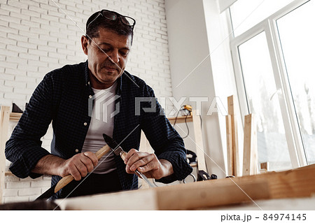 Middle-aged man carpenter working in a workshop with chisel and hammer 84974145