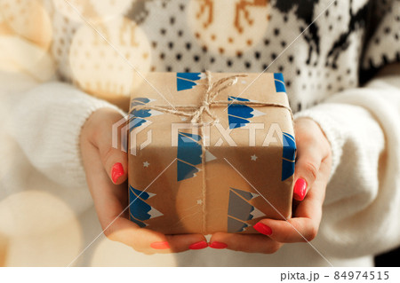 Female hands in sweater holding wrapped Christmas gift Female hands in sweater holding wrapped Christmas gift 84974515