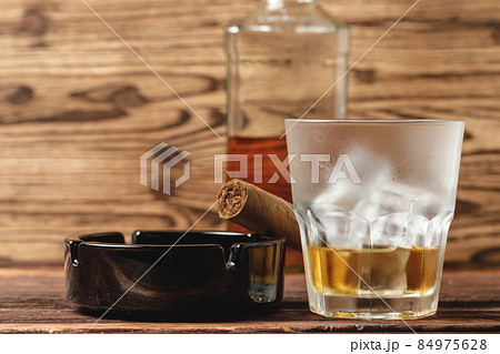 Glass of whiskey and rolled cigars on wooden table Glass of whiskey and rolled cigars on wooden table 84975628