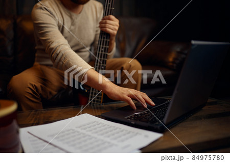 Young man learning playing guitar through internet 84975780
