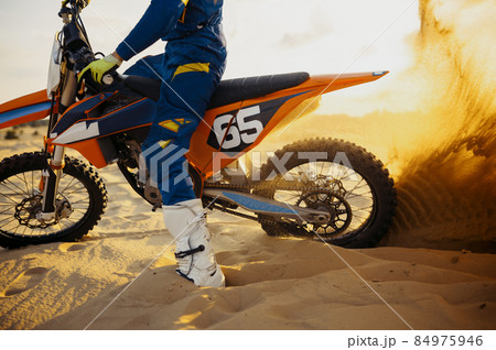 Motocross rider skidding wheel raising sand dust 84975946