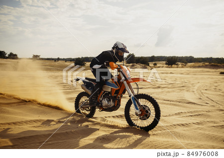 Professional motocross rider driving on sand dune 84976008