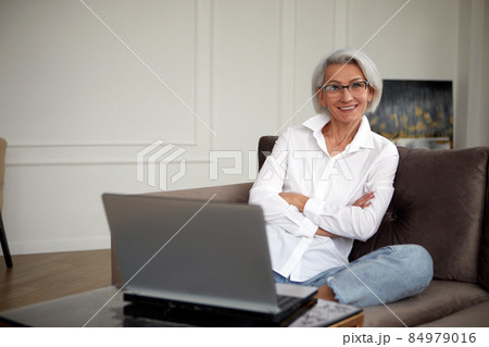 Positive woman entrepreneur sitting on armchair while working on laptop Positive woman entrepreneur sitting on armchair while working on laptop 84979016