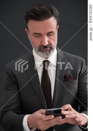 Portrait of adult businessman wearing trendy suit and sitting in modern studio on stylish chair against the black background 84979180
