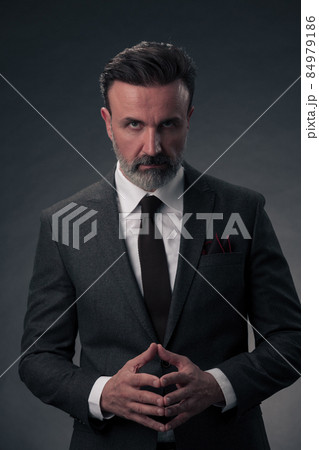 Portrait of a stylish elegant senior businessman with a beard and casual business clothes in photo studio isolated on dark background gesturing with hands Portrait of a stylish elegant senior businessman with a beard and casual business clothes in photo studio isolated on dark background gesturing with hands 84979186