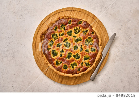 Quiche pie with broccoli, tuna and cheese on round wooden cutting board with knife 84982018