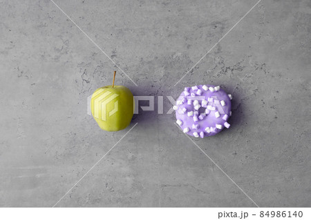 Useful and unhealthy food concept. Green apple and donut on gray concrete background Useful and unhealthy food concept. Green apple and donut on gray concrete background 84986140