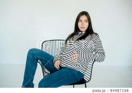 Pregnant attractive woman sits on a chair in the studio. 84987198