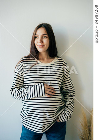 Vertical portrait of a young pregnant woman in a striped sweatshirt. 84987209