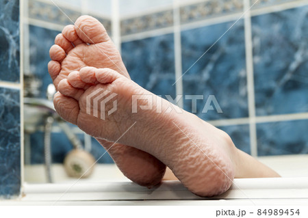 Wrinkled bare feet coming out from a bathtub. Young person getting a bath feet close-up indoor in bathroom interrior photo Wrinkled bare feet coming out from a bathtub. Young person getting a bath feet close-up indoor in bathroom interrior photo 84989454