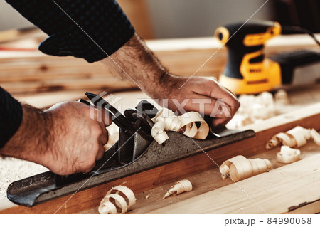 Carpenter's hands planing a plank of wood with a hand plane Carpenter's hands planing a plank of wood with a hand plane 84990068