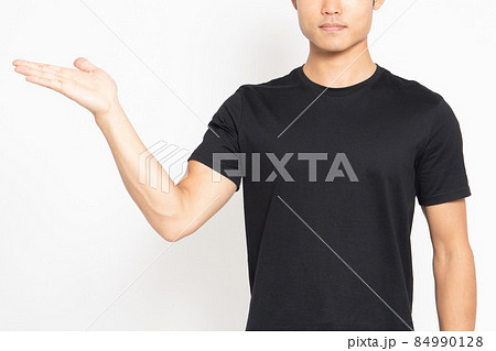 白い背景の前に立って、案内のポーズをする黒いTシャツを着ている男性 84990128