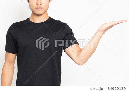 白い背景の前に立って、案内のポーズをする黒いTシャツを着ている男性 84990129
