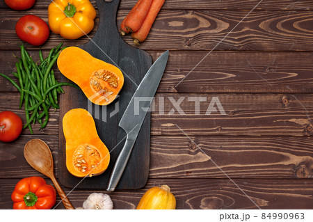 Small pumpkin cut into halves on wooden cutting board with knife 84990963