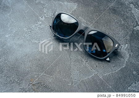 Dark male sunglasses on grey concrete surface Dark male sunglasses on grey concrete surface 84991050