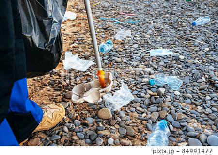 Close up photo of a man collecting garbage with a grabbing tool on the beach Close up photo of a man collecting garbage with a grabbing tool on the beach 84991477