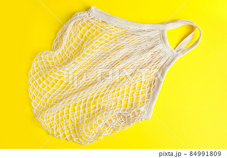 Eco-friendly mesh bag on a yellow background. Recyclable organic cotton bag. Sustainable lifestyle and shopping. Eco-friendly mesh bag on a yellow background. Recyclable organic cotton bag. Sustainable lifestyle and shopping. 84991809